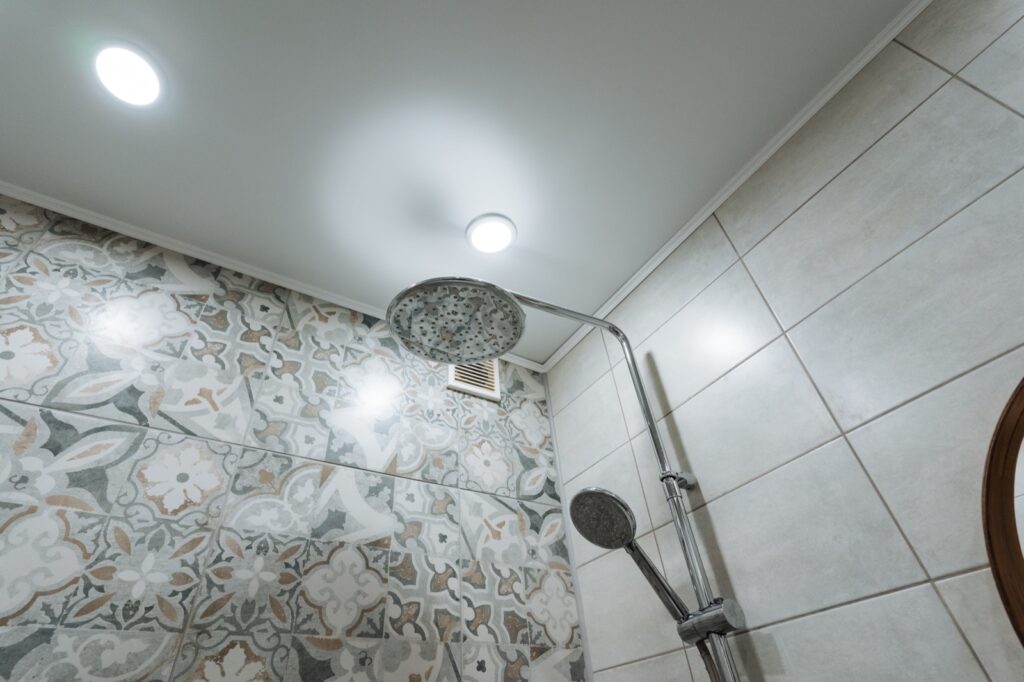 Clean tiled shower with a ceiling exhaust vent above the shower head