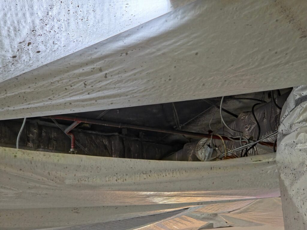 Crawl space with a plastic vapor barrier over the ground and pipes running overhead